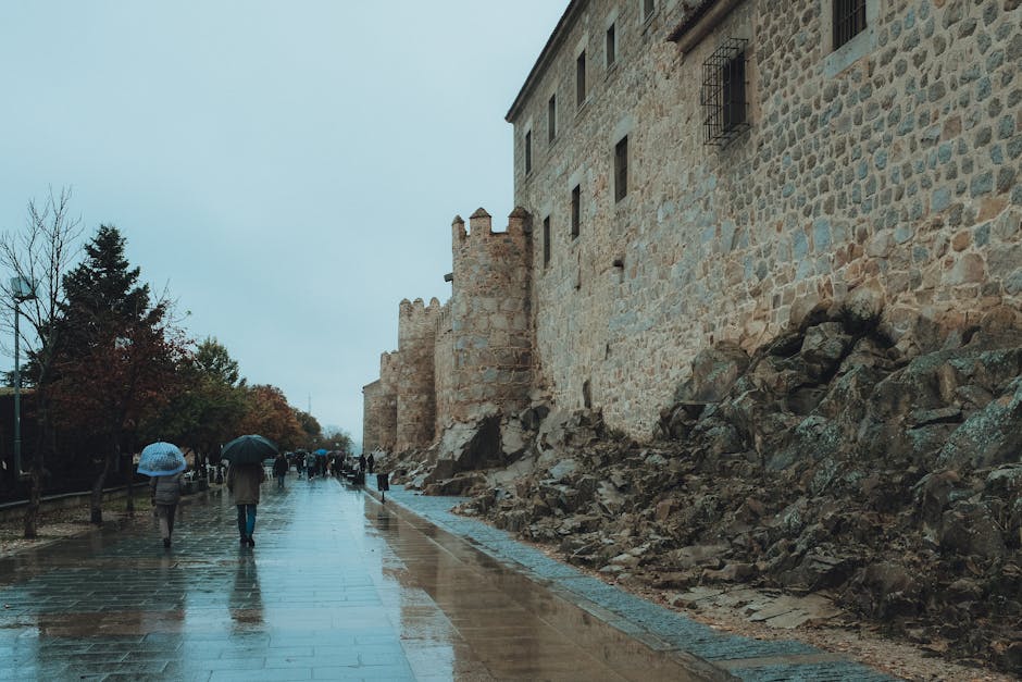 People walking along wet streets by the ancient walls of Ávila, Spain.
