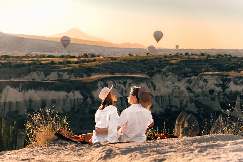 A couple sits in Cappadocia, watching hot air balloons at sunset